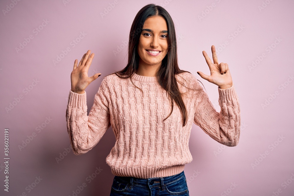Young beautiful brunette woman wearing casual sweater over isolated pink background showing and pointing up with fingers number eight while smiling confident and happy.