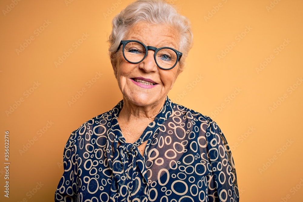 Senior beautiful grey-haired woman wearing casual shirt and glasses over yellow background with a happy and cool smile on face. Lucky person. Senior beautiful grey-haired woman wearing casual shirt and glasses over yellow background with a happy and cool smile on face. Lucky person.