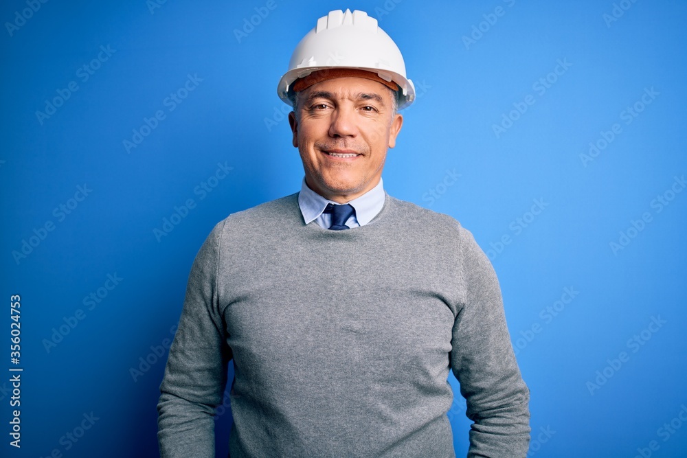 Middle age handsome grey-haired engineer man wearing safety helmet over blue background with a happy and cool smile on face. Lucky person. Middle age handsome grey-haired engineer man wearing safety helmet over blue background with a happy and cool smile on face. Lucky person.