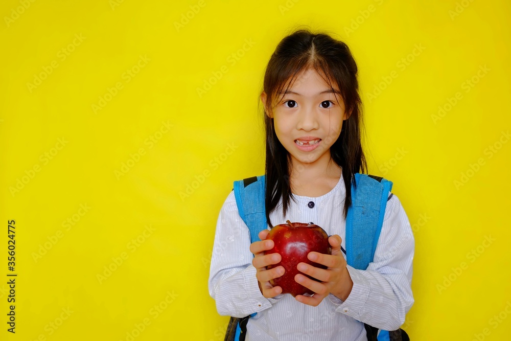 A cute young Asian girl holding up an apple, getting ready to eat it for breakfast. Bright yellow background. A cute young Asian girl holding up an apple, getting ready to eat it for breakfast. Bright yellow background.