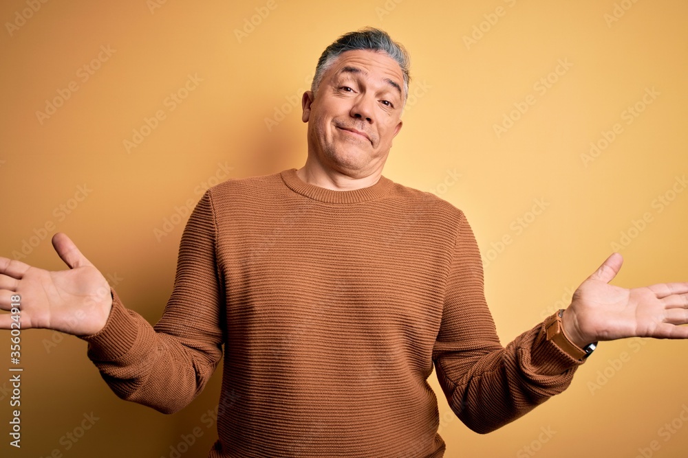 Middle age handsome grey-haired man wearing casual sweater over yellow background clueless and confused expression with arms and hands raised. Doubt concept. Middle age handsome grey-haired man wearing casual sweater over yellow background clueless and confused expression with arms and hands raised. Doubt concept.