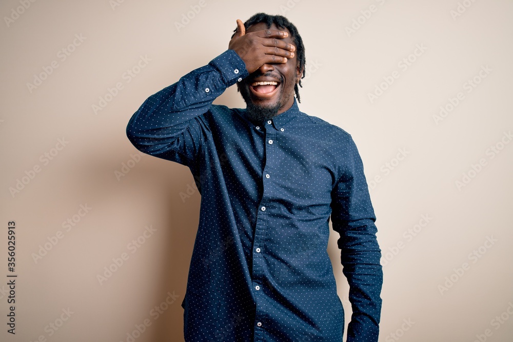 Young handsome african american man wearing casual shirt standing over white background smiling and laughing with hand on face covering eyes for surprise. Blind concept. Young handsome african american man wearing casual shirt standing over white background smiling and laughing with hand on face covering eyes for surprise. Blind concept.
