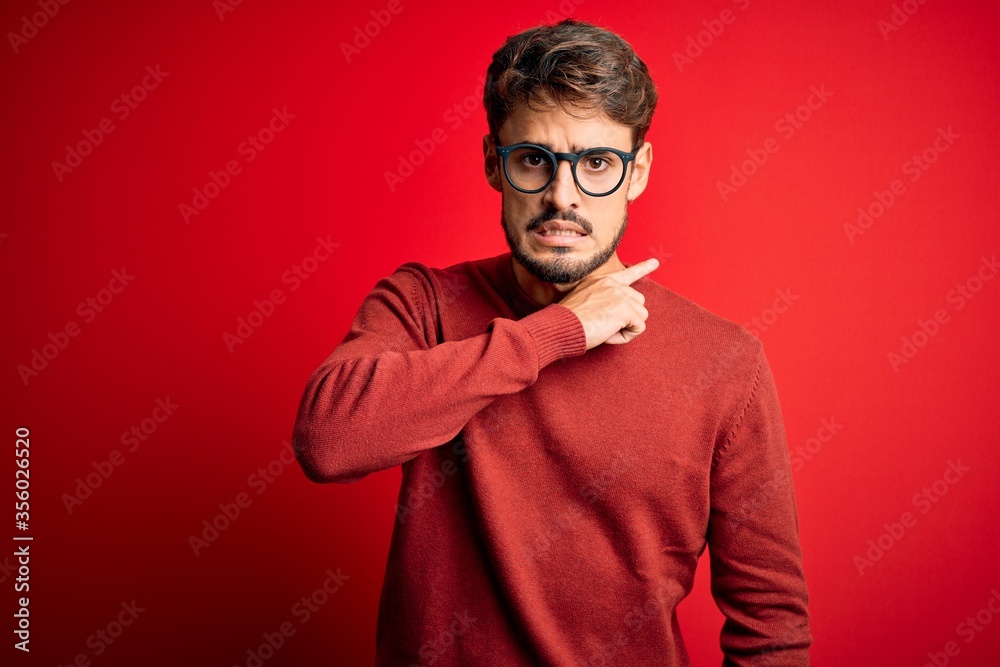 Young handsome man with beard wearing glasses and sweater standing over red background cutting throat with hand as knife, threaten aggression with furious violence Young handsome man with beard wearing glasses and sweater standing over red background cutting throat with hand as knife, threaten aggression with furious violence