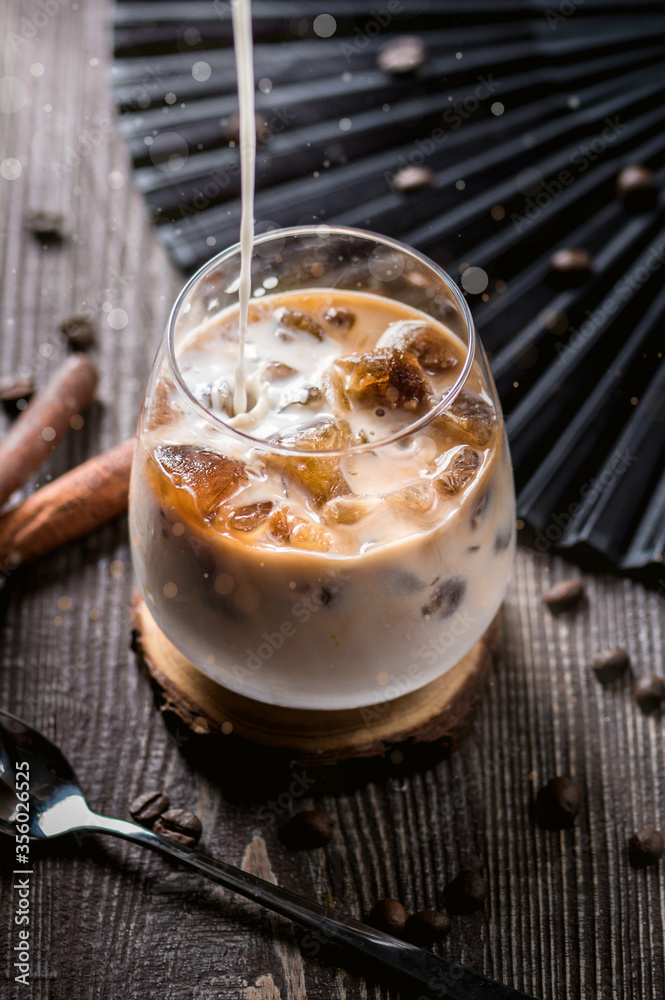 Ice coffee with cream poured over and coffee beans on a old rustic wooden table Ice coffee with cream poured over and coffee beans on a old rustic wooden table