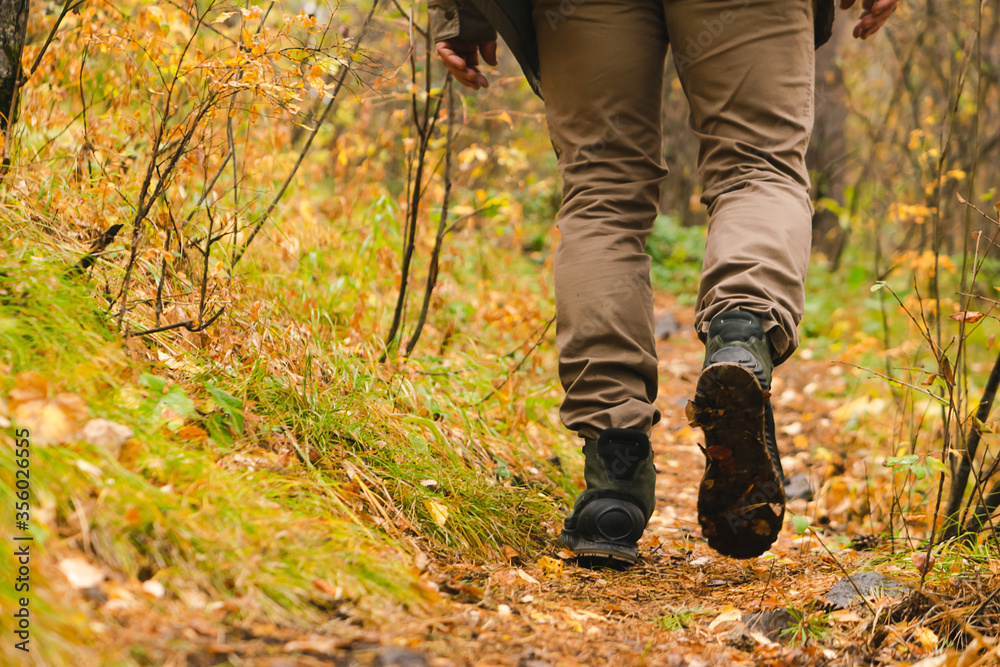 A man traveler walks along forest path in hiking boots. Tourism and adventure concept. Horizontal frame