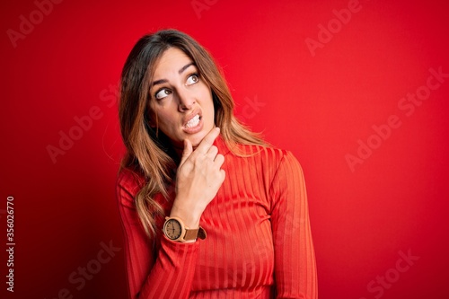 Young beautiful brunette woman wearing casual turtleneck sweater over red background Thinking worried about a question, concerned and nervous with hand on chin © Krakenimages.com