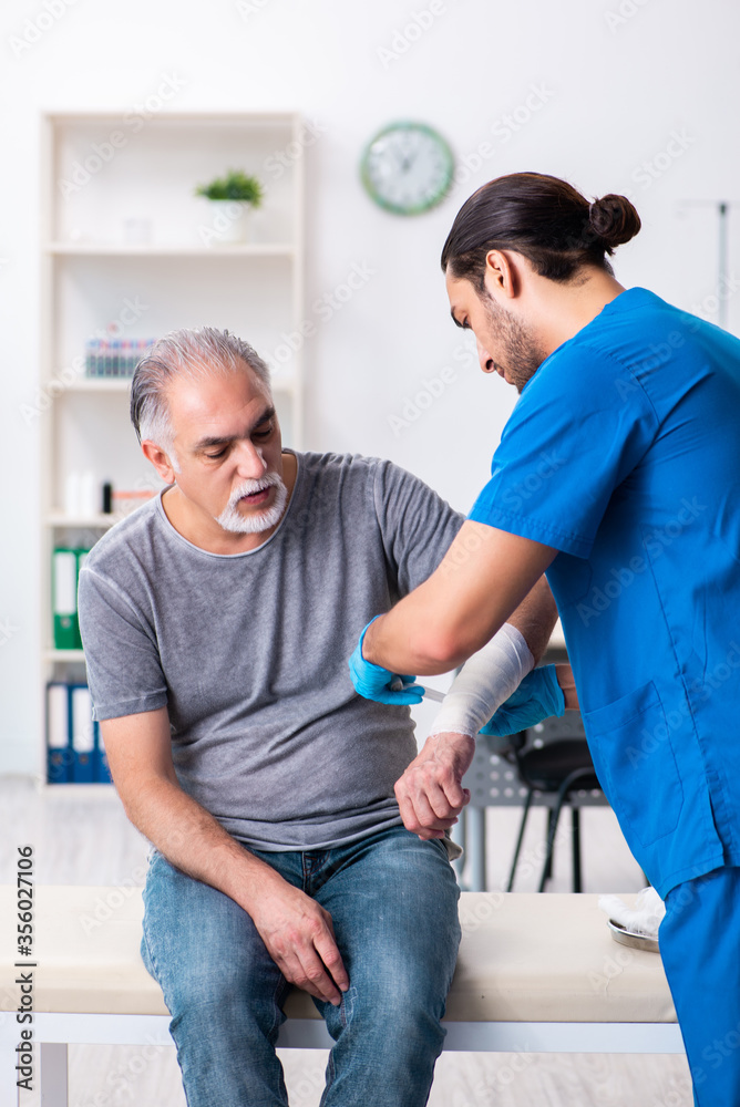 Fototapeta premium Young male doctor and old patient in first aid concept