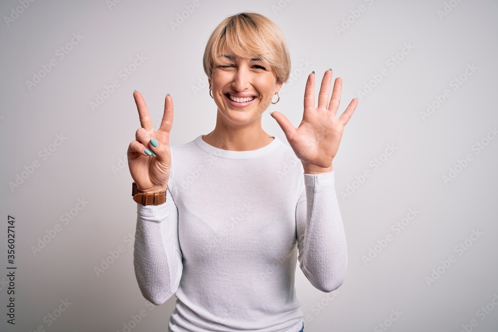 Young beautiful blonde woman with modern short hair hairstyle standing over isolated background showing and pointing up with fingers number seven while smiling confident and happy. Young beautiful blonde woman with modern short hair hairstyle standing over isolated background showing and pointing up with fingers number seven while smiling confident and happy.