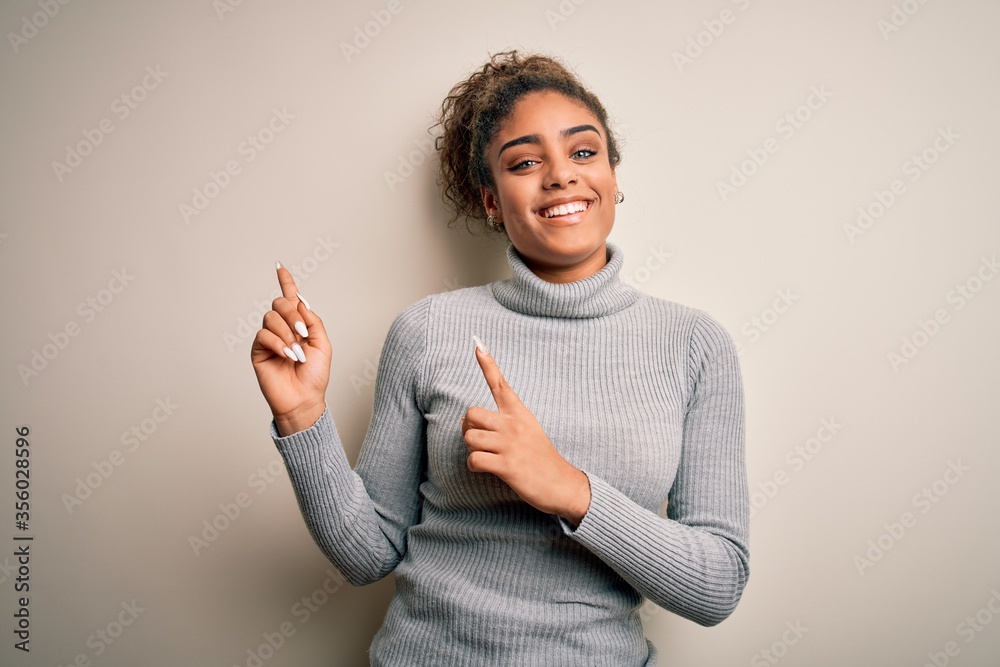 Beautiful african american girl wearing turtleneck sweater standing over white background smiling and looking at the camera pointing with two hands and fingers to the side. Beautiful african american girl wearing turtleneck sweater standing over white background smiling and looking at the camera pointing with two hands and fingers to the side.