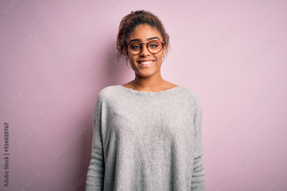 Young beautiful african american girl wearing sweater and glasses over pink background with a happy and cool smile on face. Lucky person. Young beautiful african american girl wearing sweater and glasses over pink background with a happy and cool smile on face. Lucky person.