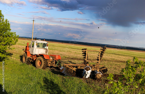  tractor plows and harrows  land in  large field on  sunny spring day. preparing  soil for planting crops, plowing  soil with  tractor with  disk plow.