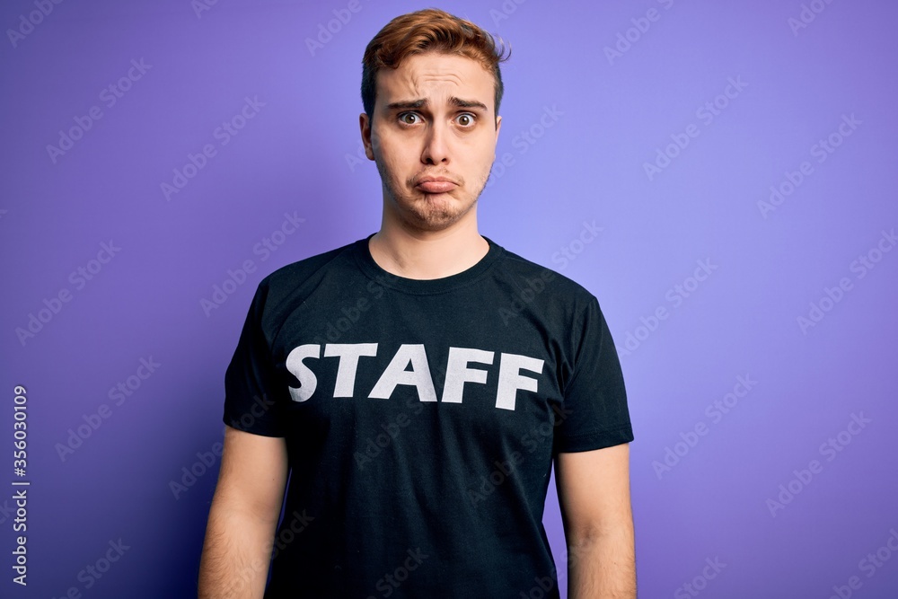 Young handsome redhead worker man wearing staff t-shirt uniform over purple background depressed and worry for distress, crying angry and afraid. Sad expression.