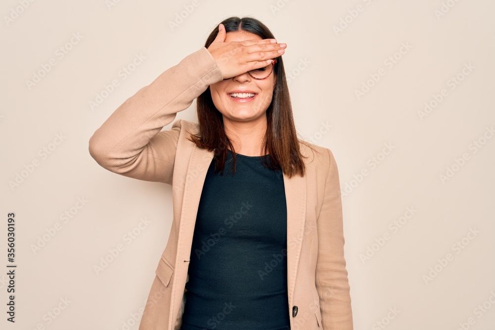 Φωτογραφία Young beautiful brunette businesswoman wearing jacket and glasses over white background smiling and laughing with hand on face covering eyes for surprise