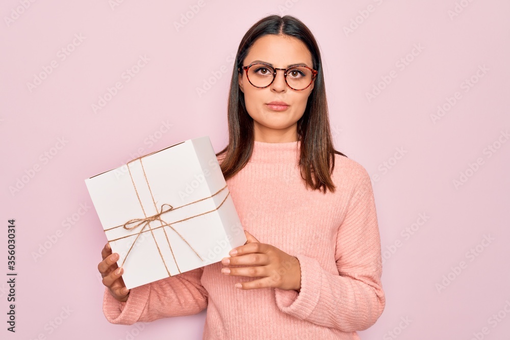 Φωτογραφία Young beautiful brunette woman holding birthday gift over isolated pink backgrou