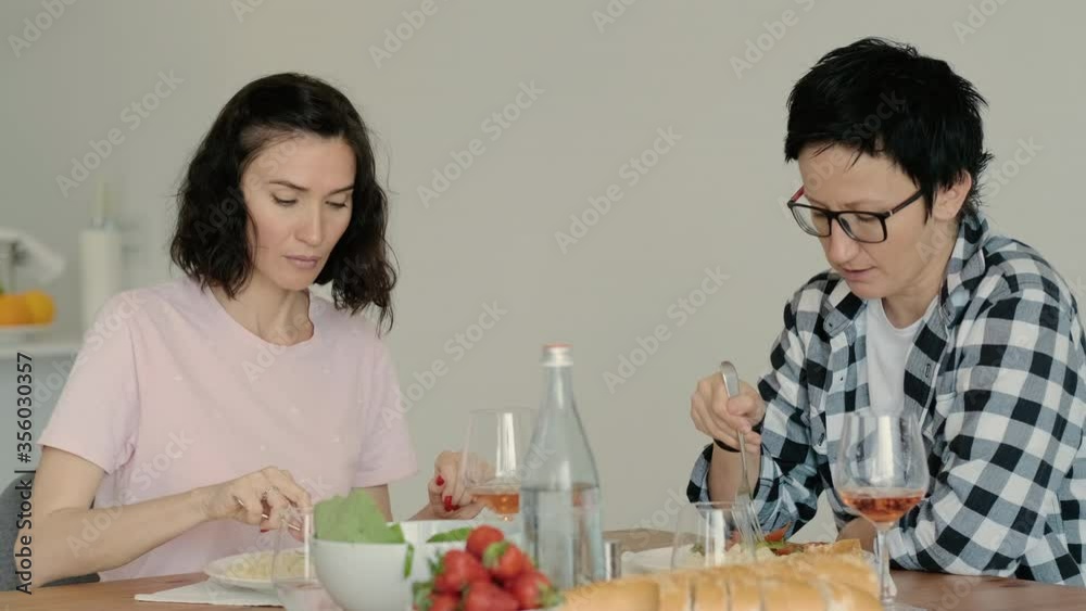 female lesbian couple eating at table having healthy food on kitchen and wine Rbbro. adult women eat organic vegan breakfast at morning and chatting. modern home interior. lgbt girlfriend female lesbian couple eating at table having healthy food on kitchen and wine Rbbro. adult women eat organic vegan breakfast at morning and chatting. modern home interior. lgbt girlfriend