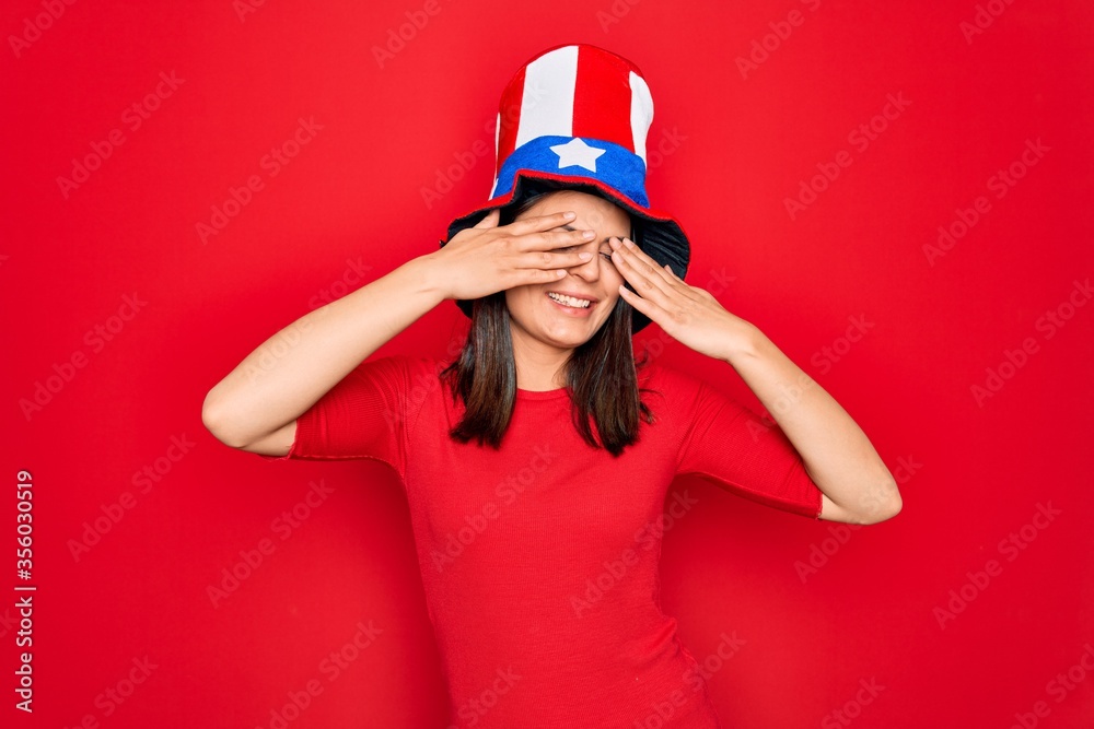 Young beautiful brunette woman wearing united states hat celebrating independence day covering eyes with hands smiling cheerful and funny. Blind concept. Young beautiful brunette woman wearing united states hat celebrating independence day covering eyes with hands smiling cheerful and funny. Blind concept.