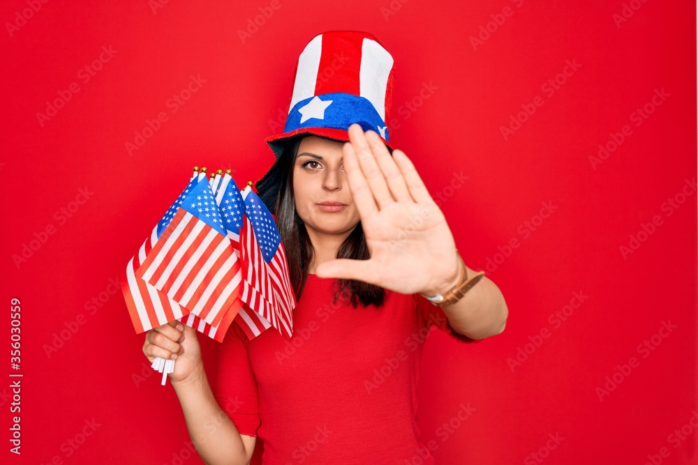 Φωτογραφία Young beautiful brunette patriotic woman wearing united states hat holding usa f