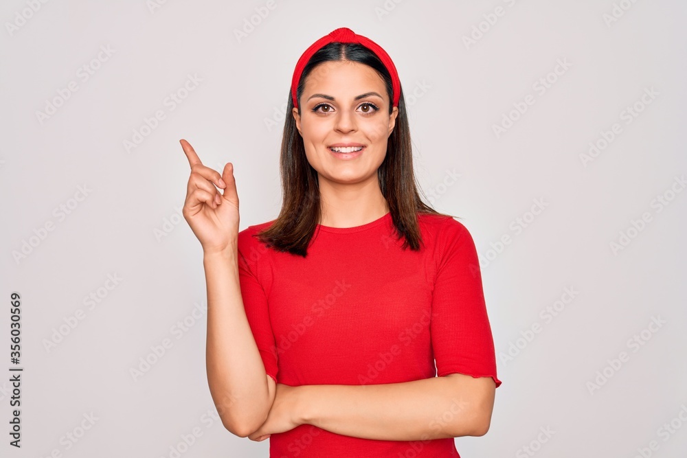 Young beautiful brunette woman wearing casual t-shirt and diadem over white background with a big smile on face, pointing with hand and finger to the side looking at the camera. Young beautiful brunette woman wearing casual t-shirt and diadem over white background with a big smile on face, pointing with hand and finger to the side looking at the camera.