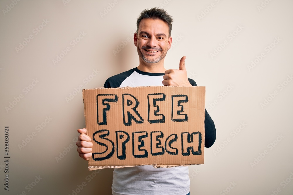 Young handsome man asking for rights holding banner with free speech message happy with big smile doing ok sign, thumb up with fingers, excellent sign Young handsome man asking for rights holding banner with free speech message happy with big smile doing ok sign, thumb up with fingers, excellent sign