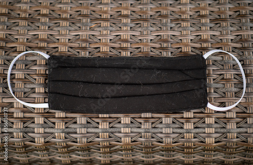 DIY black homemade cotton face mask laying on a brown wicker chair. Corona virus handmade preventive equipment  