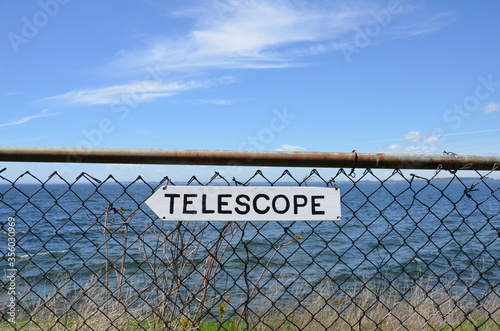 white telescope sign on metal fence and ocean