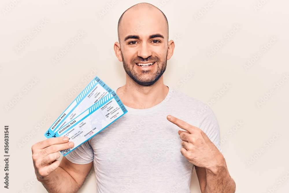 Young handsome bald man holding airline boarding pass smiling happy pointing with hand and finger Young handsome bald man holding airline boarding pass smiling happy pointing with hand and finger