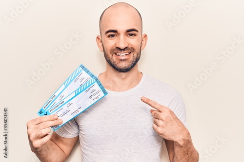Young handsome bald man holding airline boarding pass smiling happy pointing with hand and finger photo