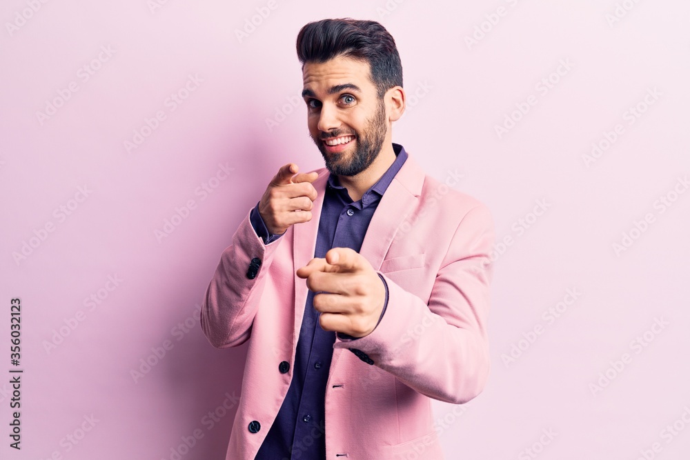 Young handsome man with beard wearing elegant jacket pointing fingers to camera with happy and funny face. good energy and vibes. Young handsome man with beard wearing elegant jacket pointing fingers to camera with happy and funny face. good energy and vibes.
