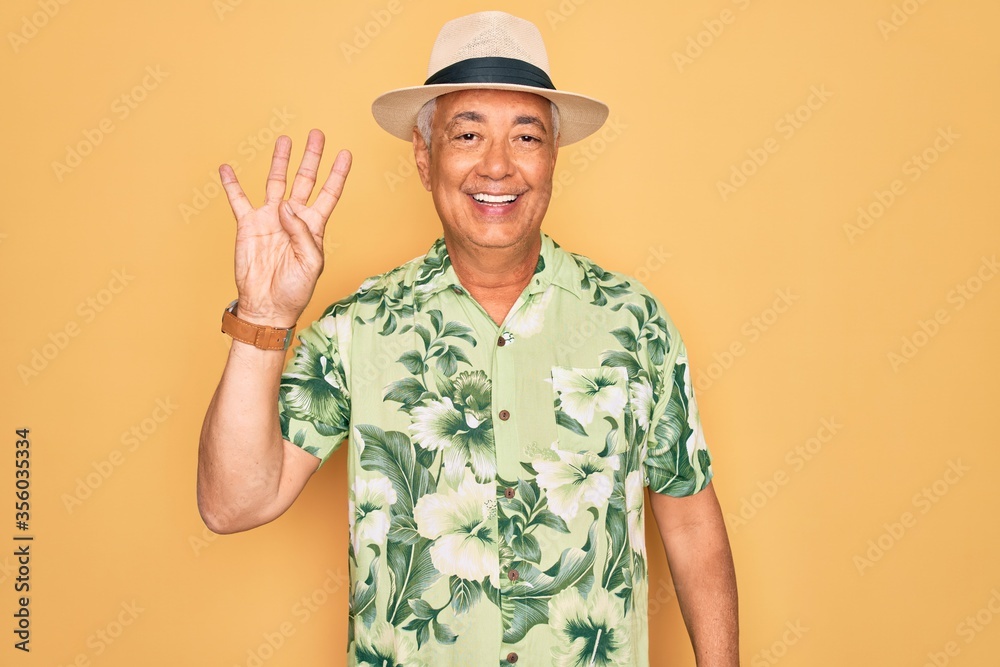 Middle age senior grey-haired man wearing summer hat and floral shirt on beach vacation showing and pointing up with fingers number four while smiling confident and happy.