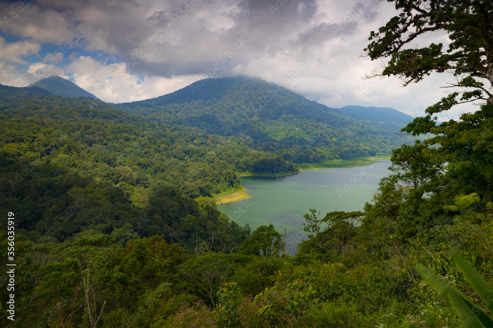 Panoramic landscape. Scenic view to the lake surrounded by hills, mountails and tropical rainforest. Bright sunlight. Buyan lake in Bedugul, Bali, Indonesia