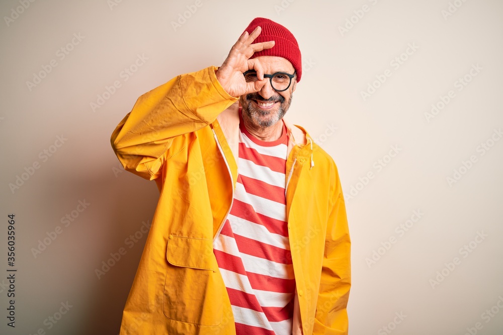 Middle age hoary man wearing glasses and rain coat standing over isolated white background doing ok gesture with hand smiling, eye looking through fingers with happy face. Middle age hoary man wearing glasses and rain coat standing over isolated white background doing ok gesture with hand smiling, eye looking through fingers with happy face.