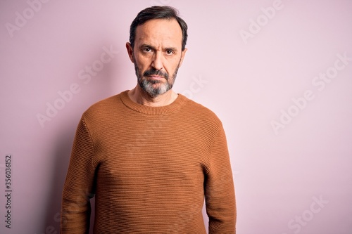 Middle age hoary man wearing casual brown sweater standing over isolated pink background with serious expression on face. Simple and natural looking at the camera.
