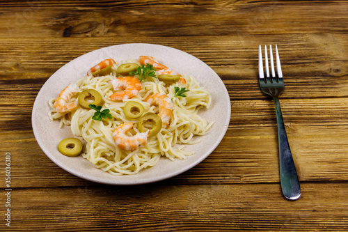Spaghetti pasta with prawns, green olives and parsley on wooden table