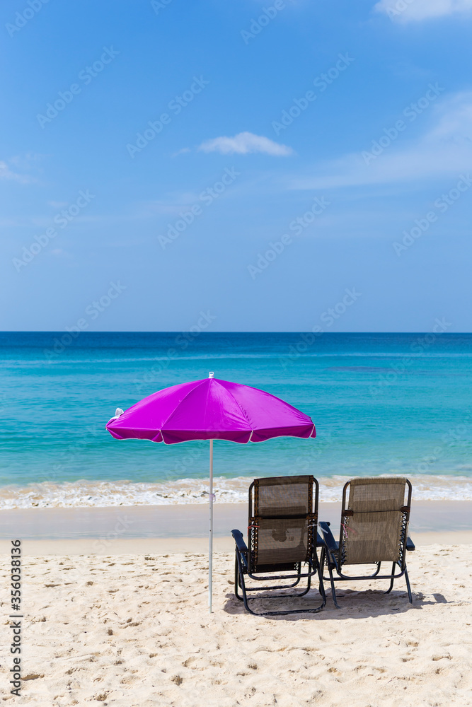 Beach chairs under pink umbrella on sand beach with beautiful blue sea and clear blue sky view, relaxing by the beach, summer outdoor day light, holiday break