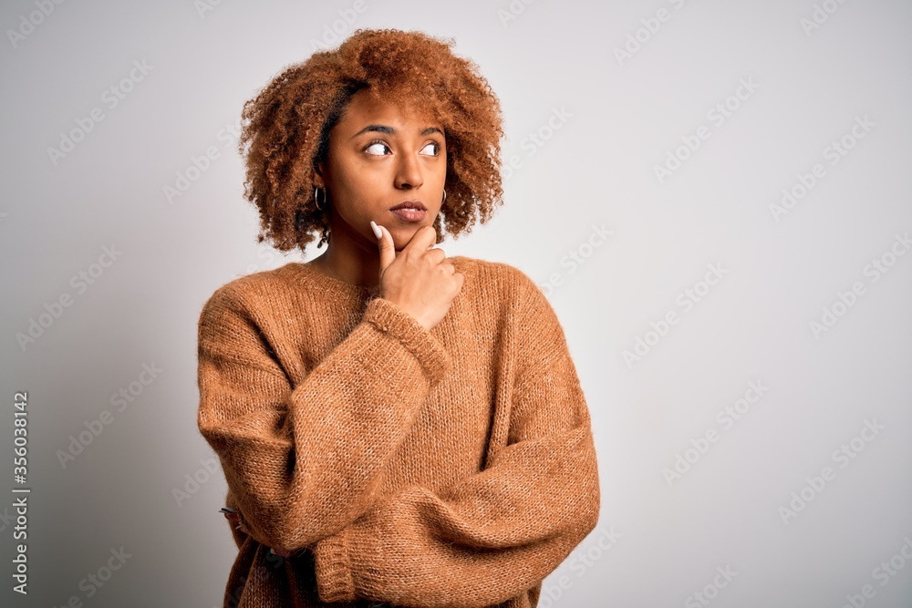 Young beautiful African American afro woman with curly hair wearing casual sweater with hand on chin thinking about question, pensive expression. Smiling with thoughtful face. Doubt concept. Young beautiful African American afro woman with curly hair wearing casual sweater with hand on chin thinking about question, pensive expression. Smiling with thoughtful face. Doubt concept.