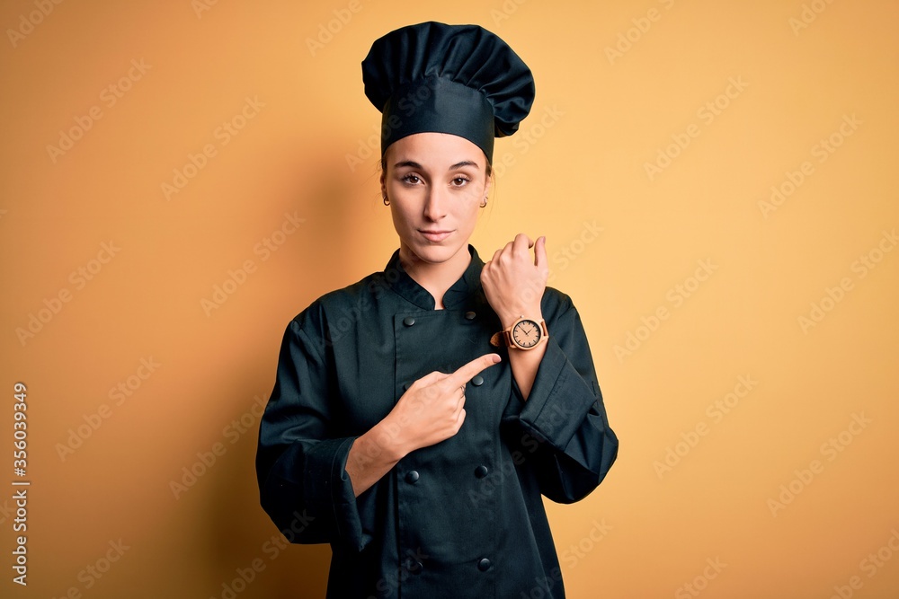 Young beautiful chef woman wearing cooker uniform and hat standing over yellow background In hurry pointing to watch time, impatience, looking at the camera with relaxed expression Young beautiful chef woman wearing cooker uniform and hat standing over yellow background In hurry pointing to watch time, impatience, looking at the camera with relaxed expression