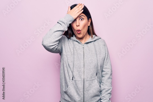 Young beautiful sporty woman wearing sportswear standing over isolated pink background surprised with hand on head for mistake, remember error. Forgot, bad memory concept. © Krakenimages.com