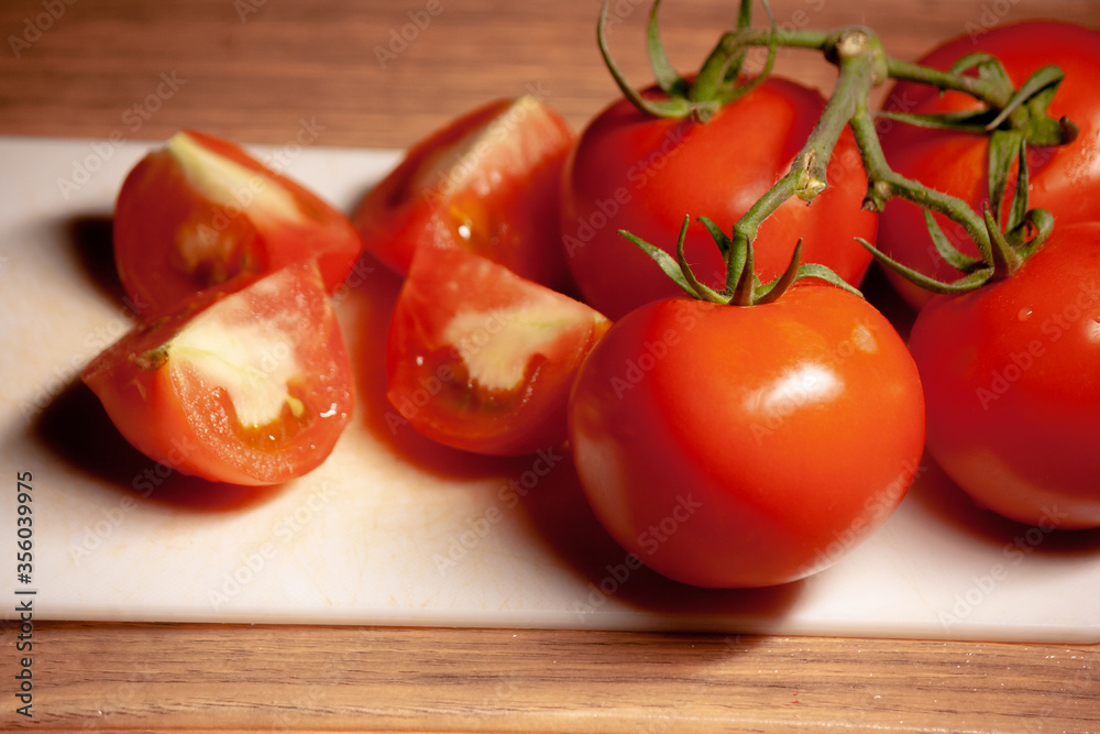 Tomato in four pieces with bunch of whole tomatoes on white chopping board food Tomato in four pieces with bunch of whole tomatoes on white chopping board food