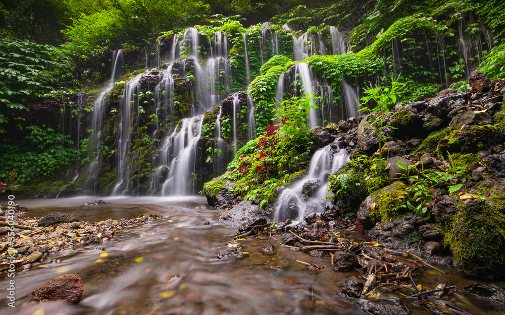 Fototapeta premium Waterfall landscape. Beautiful hidden waterfall in tropical rainforest. Nature background. Slow shutter speed, motion photography. Banyu Wana Amertha waterfall, Bali, Indonesia