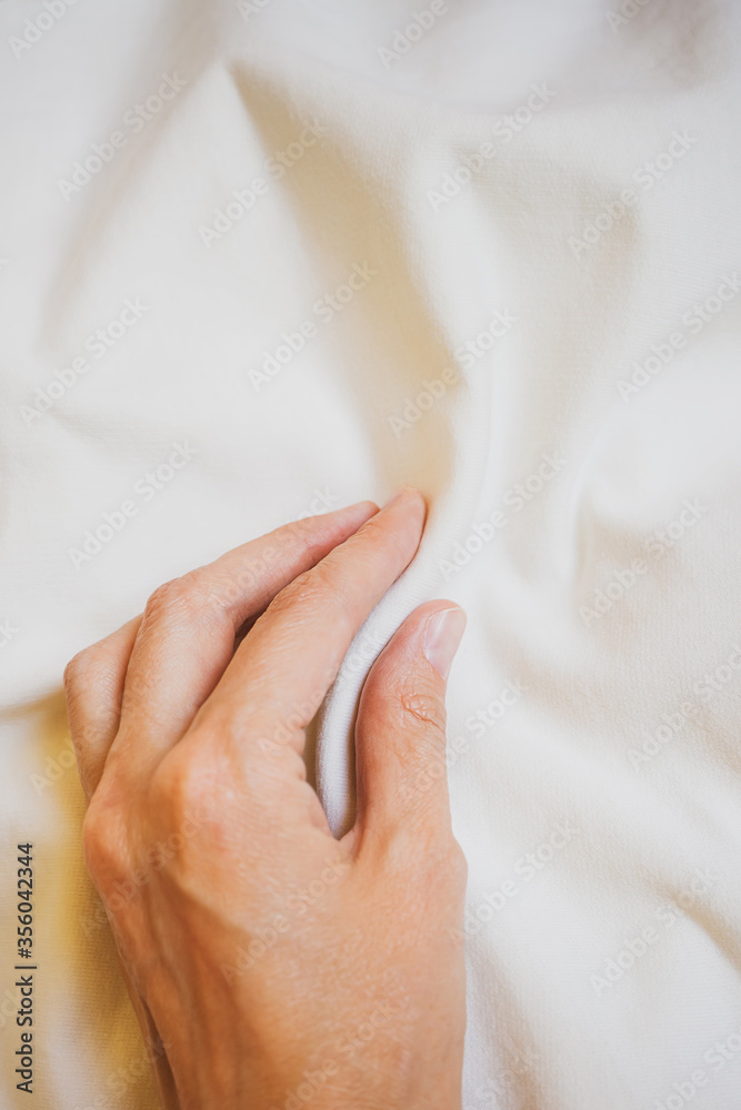 Fototapeta premium Female hand touches in light pastel fabric. The texture of the fabric. Close-up, top view, copyspace.
