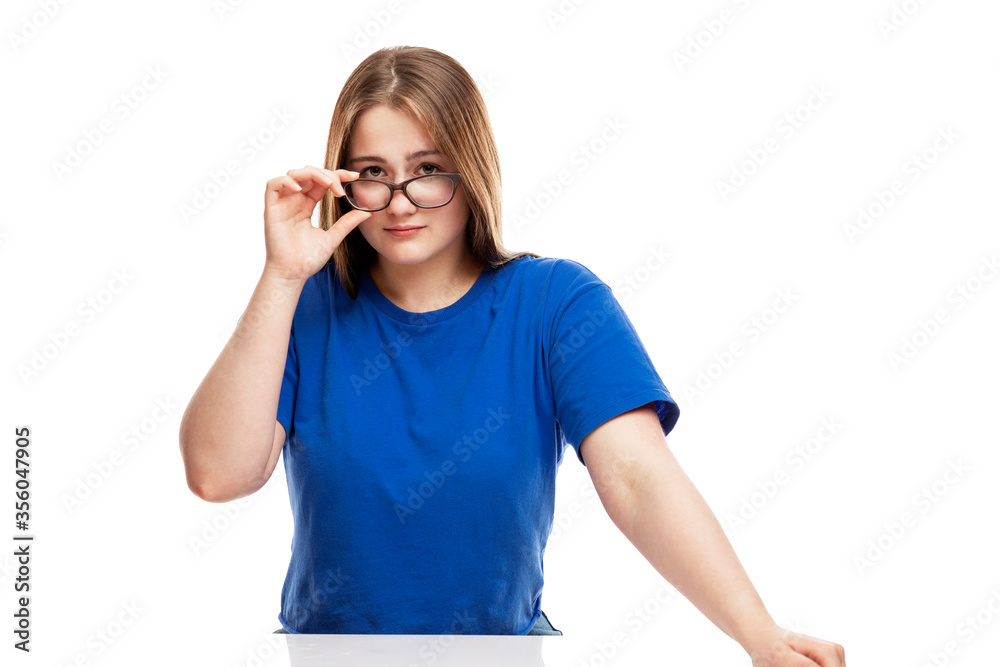 Serious young girl in a blue T-shirt adjusts his glasses. Education and knowledge. Isolated on a white background. Serious young girl in a blue T-shirt adjusts his glasses. Education and knowledge. Isolated on a white background.