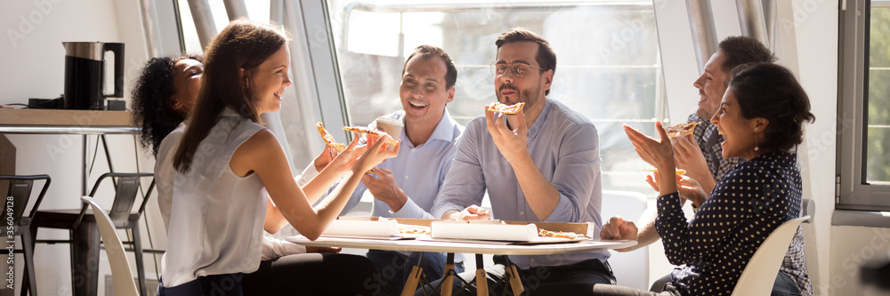 Multiethnic staff gathered together in office kitchen enjoy lunch eat pizza telling funny life stories laughing. Teambuilding corporate party concept. Horizontal photo banner for website header design - obrazy, fototapety, plakaty 