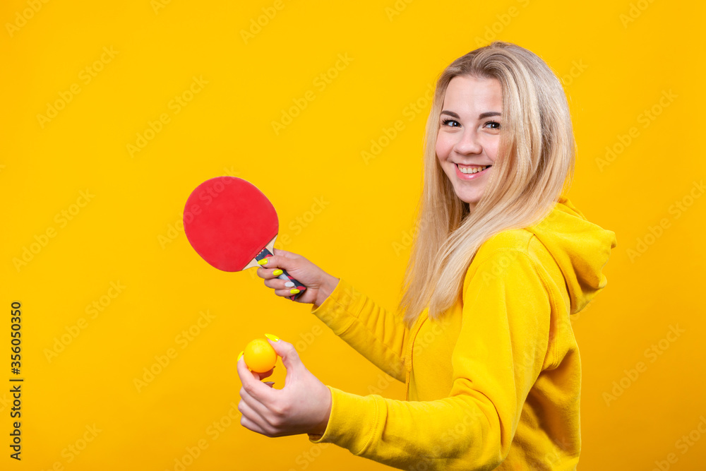 Cheerful beautiful young blonde woman in casual yellow sporty clothes play ping pong, holding a ball and racquet. Cheerful beautiful young blonde woman in casual yellow sporty clothes play ping pong, holding a ball and racquet.