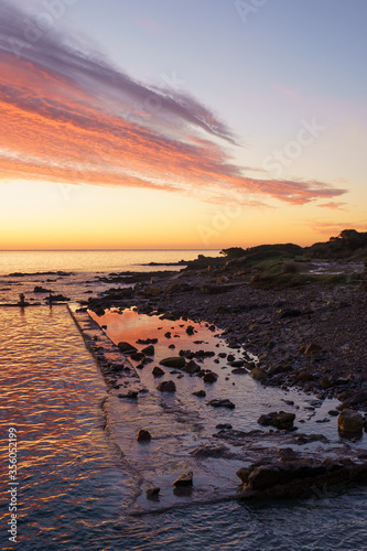 Orange and red sky with gorgeous cloud on an old abandoned sea pier in dawn or sunset with water reflections between the rocks