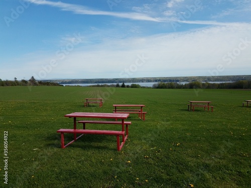 red picnic tables in green grass or field with river in Quebec, Canada