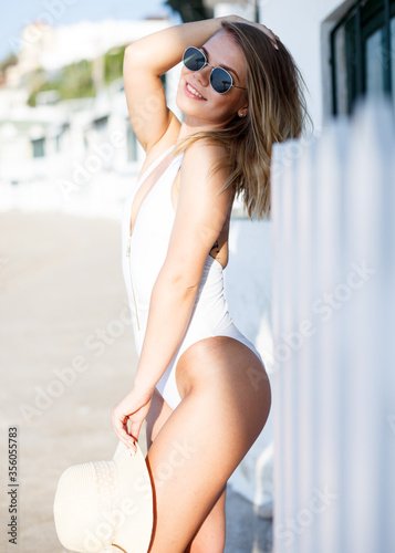 Sexy girl in swimsuit and hat playfully posing hotel wall at sea shore © JackF