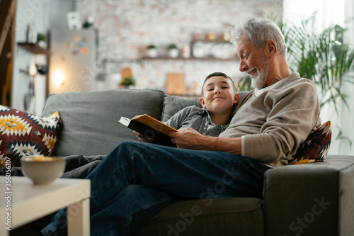 Grandfather and grandson reading a book. Grandpa and grandson enjoying at home. 