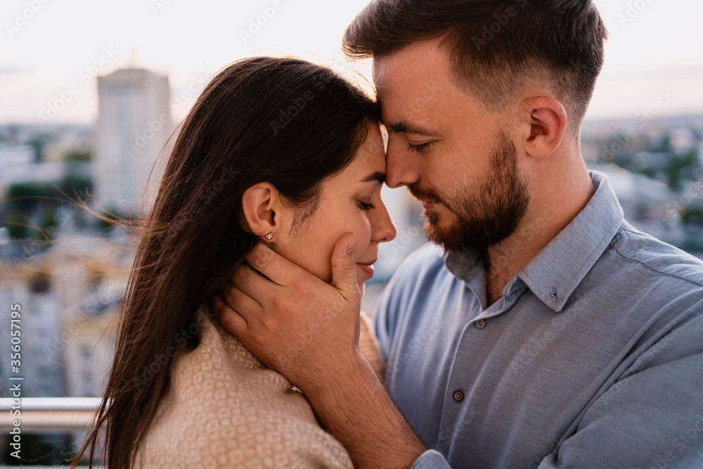 Close up portrait, man and woman smiling to each other on sunset with city in background. Couple romantic intimate moments Close up portrait, man and woman smiling to each other on sunset with city in background. Couple romantic intimate moments