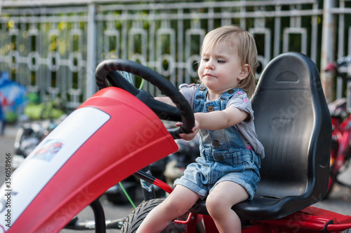 a three-year-old girl tries to drive a pedal car. 