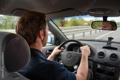 A man drives a car on the highway. He looks forward carefully and holds his hands firmly on the steering wheel. 